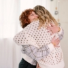 Twee vrouwen omhelzen elkaar hartelijk in een lichte, huiselijke omgeving.