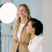 Twee vrouwen poseren lachend samen in een lichte fotostudio.