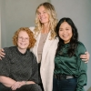 Drie vrouwen poseren samen glimlachend voor een neutrale achtergrond.