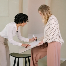 Twee vrouwen werken samen aan een ontwerp en schrijven op een groot vel papier.