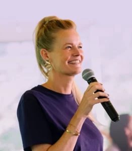 Vrouw spreekt glimlachend in een microfoon op een podium tijdens een presentatie of evenement.