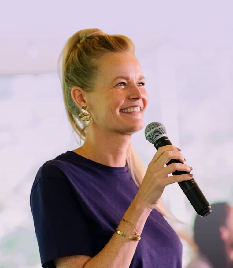 Vrouw spreekt glimlachend in een microfoon op een podium tijdens een presentatie of evenement.