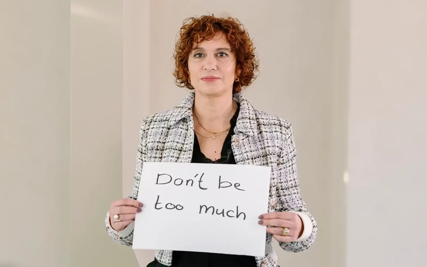 Vrouwelijke leider houdt een bord vast met de tekst "Don't be too much" als uiting van vooroordelen tegen vrouwen in leiderschap.