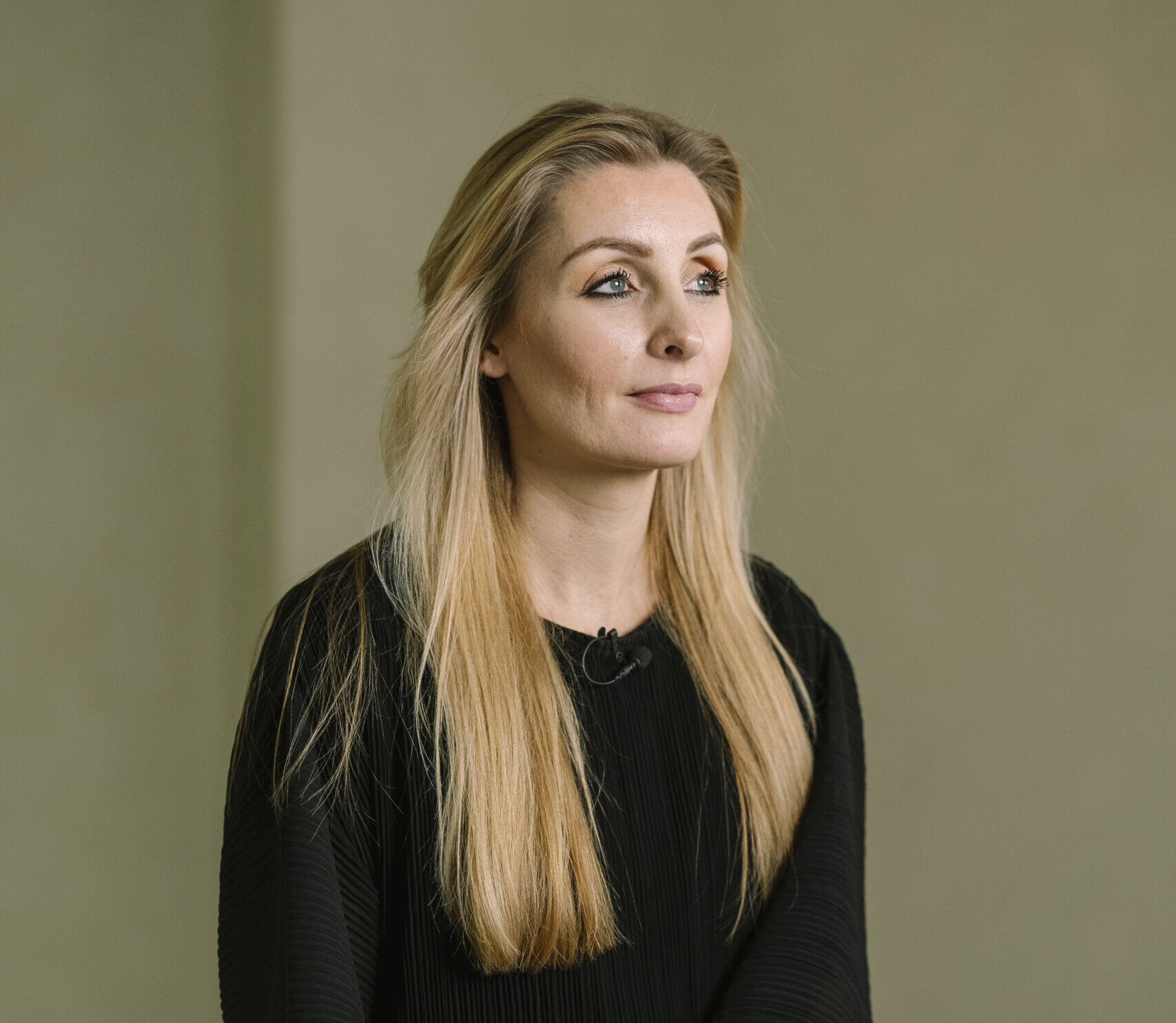 Portret van een zelfverzekerde vrouwelijk leider met lang blond haar in een zwarte outfit.