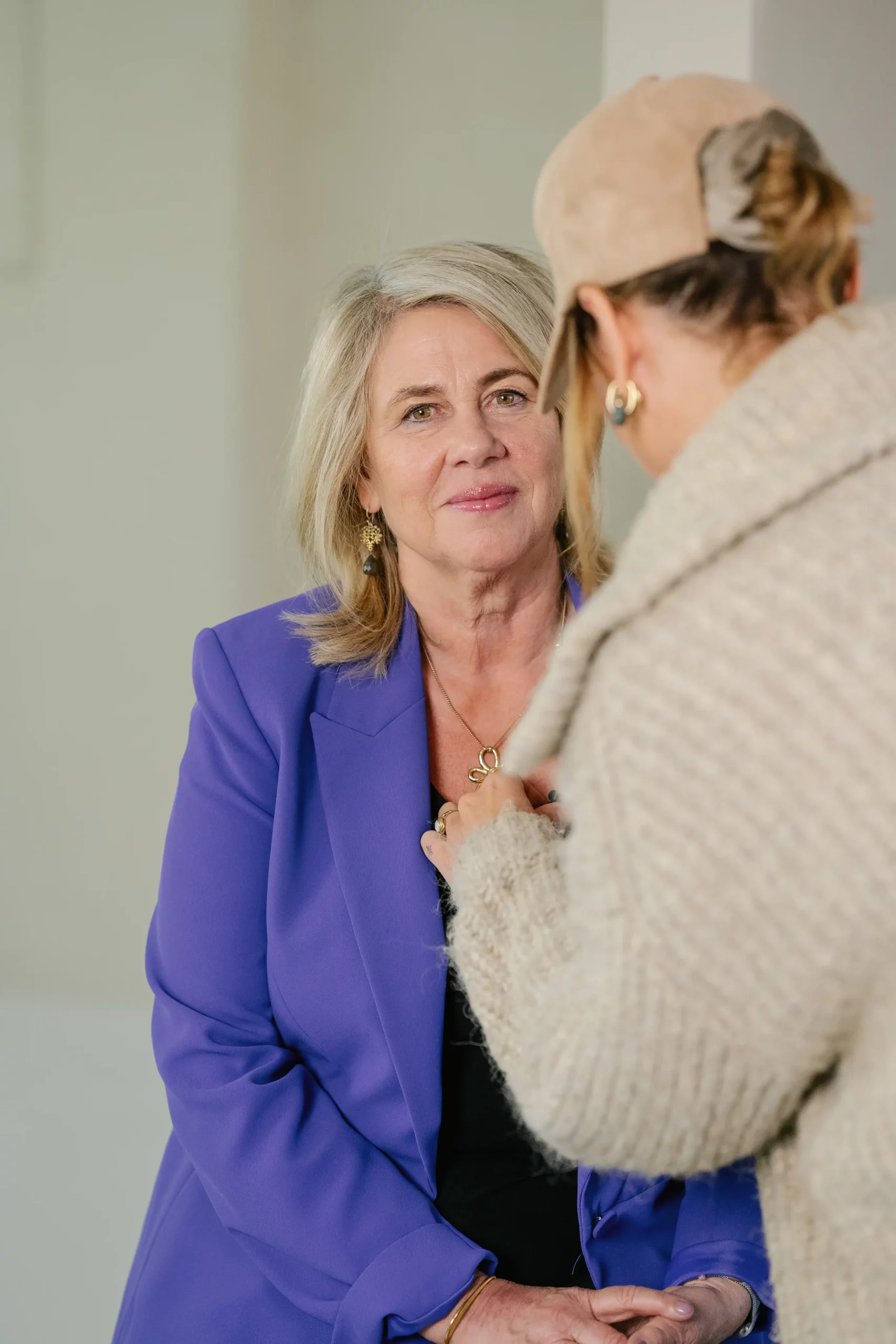 Coach vrouw in paarse blazer luistert aandachtig naar een ander persoon tijdens een gesprek.