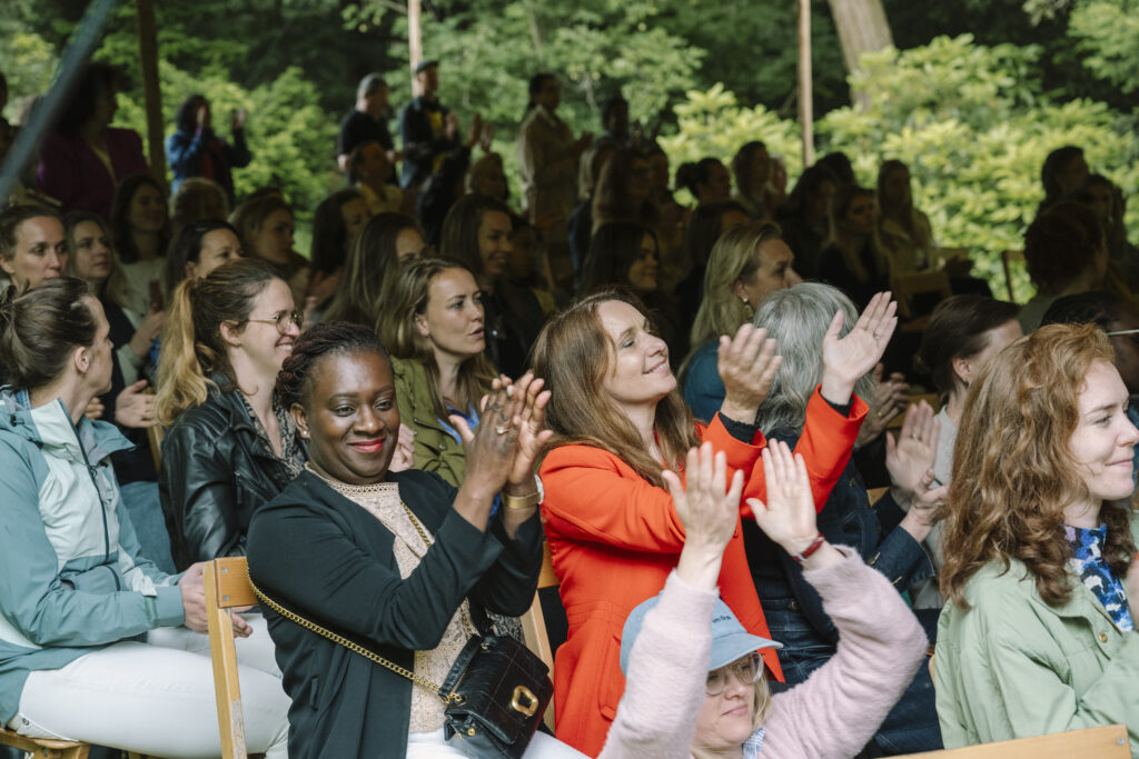 Publiek klapt enthousiast tijdens een evenement in een groene, bosrijke omgeving.