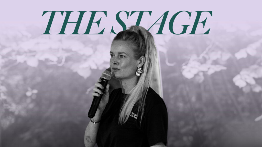 Vrouwelijk rolmodel spreekt op een podium met microfoon tijdens evenement "The Stage".