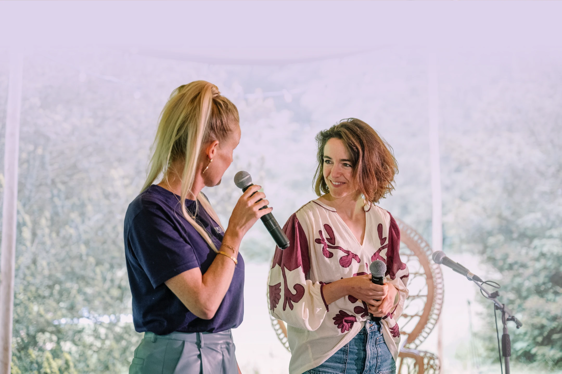 Twee vrouwen spreken met microfoons op een podium tijdens een evenement.