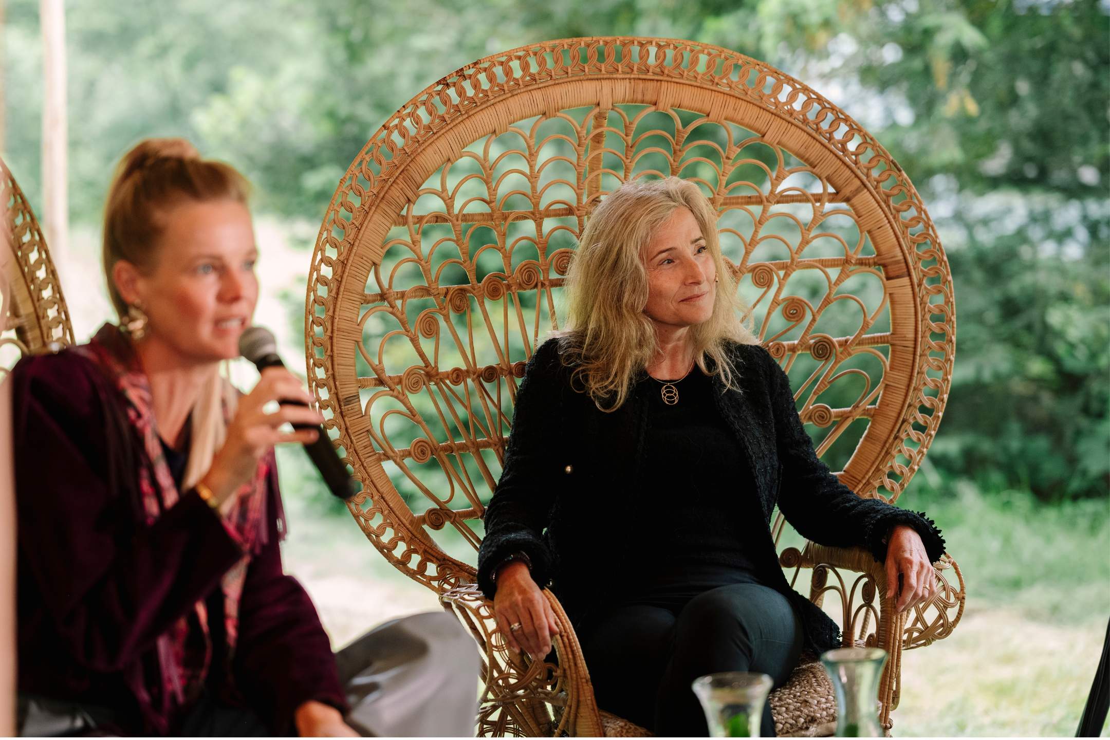 Twee vrouwen, waaronder Els van Steijn, zitten op rieten stoelen tijdens een leiderschapsevenement in een groene, natuurlijke omgeving.