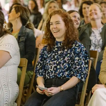 Vrouw lacht terwijl ze tussen andere bezoekers zit tijdens het New Female Leaders Festival in het House of NFL.