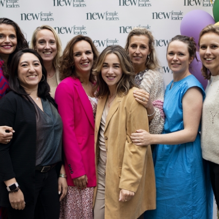 Groepsfoto van lachende vrouwen bij een event van New Female Leaders, voor een banner met het logo.