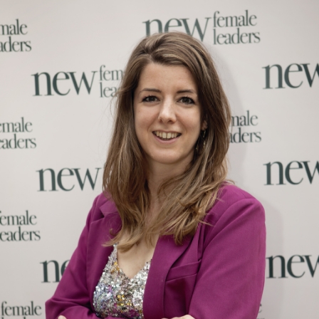 Vrouw in een paarse blazer poseert voor een muur met het logo van New Female Leaders.