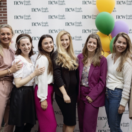 Zes lachende vrouwen poseren voor een achtergrond met het logo van New Female Leaders en kleurrijke ballonnen.