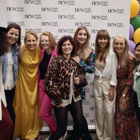 Groepsfoto van lachende vrouwen voor een backdrop van New Female Leaders tijdens een evenement.
