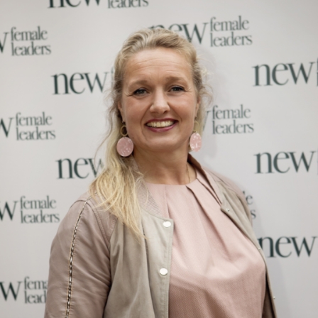 Vrouw poseert glimlachend voor een achtergrond met het logo van New Female Leaders.