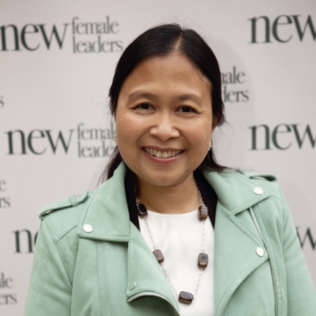Vrouw poseert glimlachend voor een achtergrond met het logo van New Female Leaders.